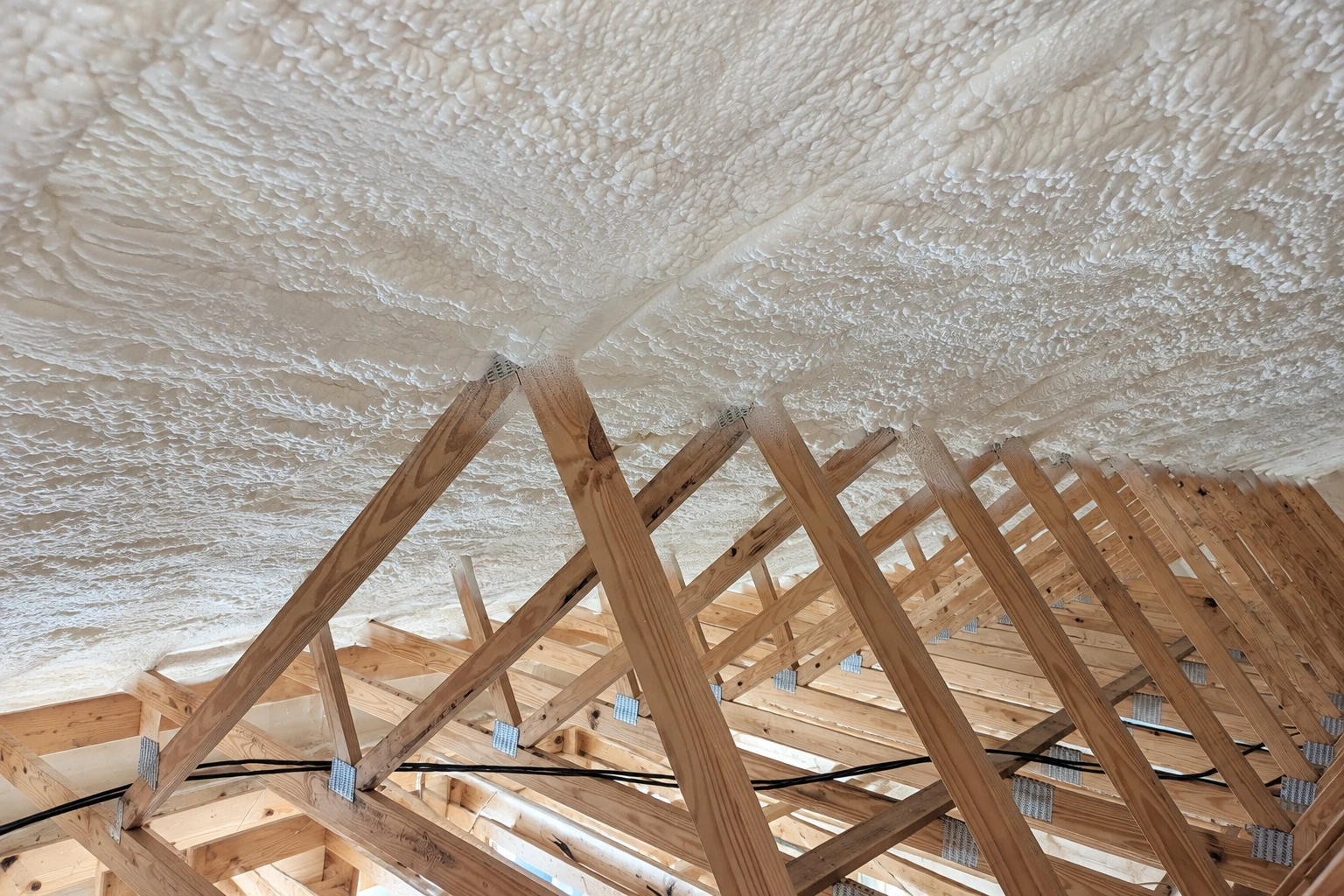 Wooden attic trusses beneath a continuous layer of white spray foam insulation.