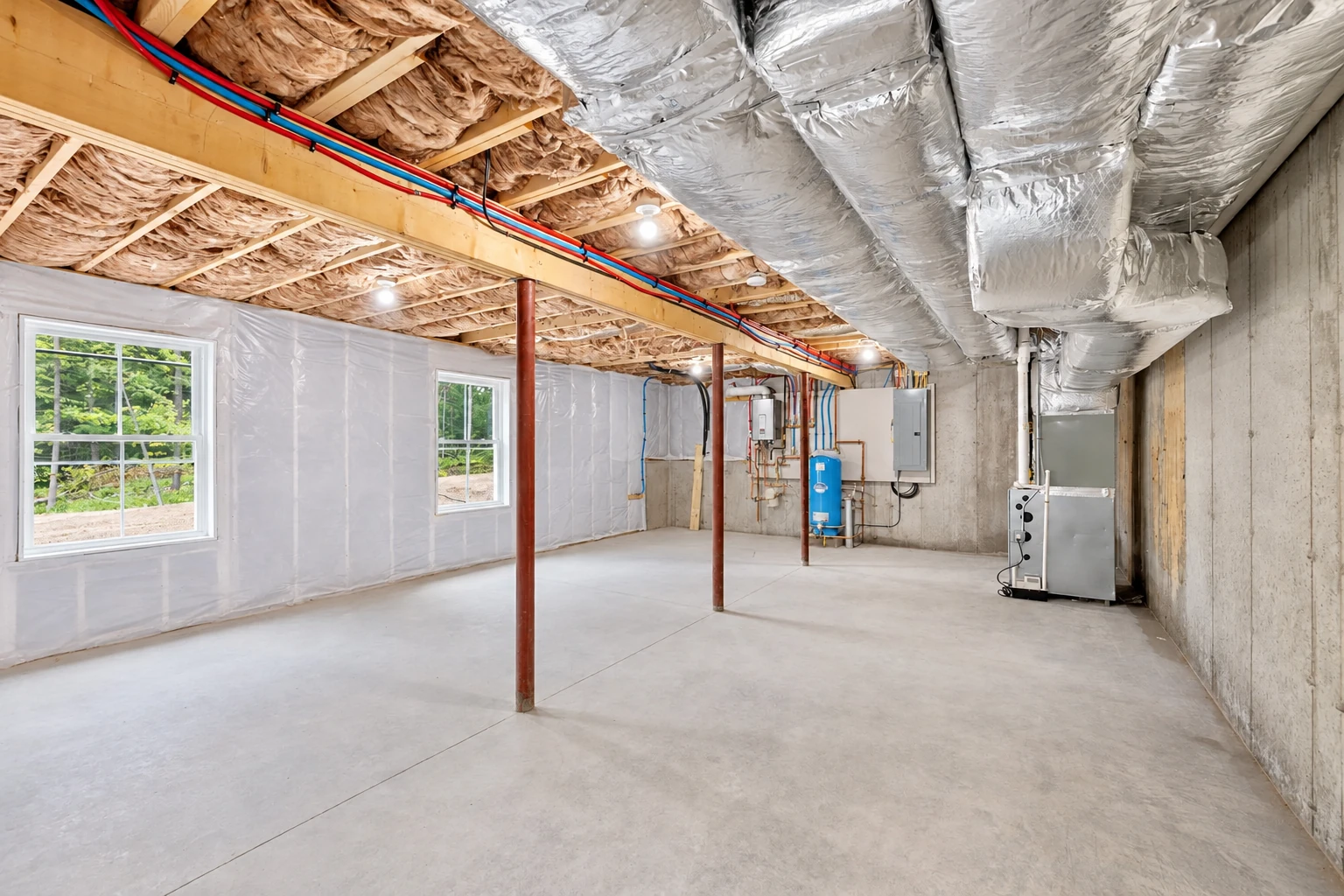 Basement with fiberglass insulation between ceiling joists, large silver HVAC ducts overhead, and a concrete floor.