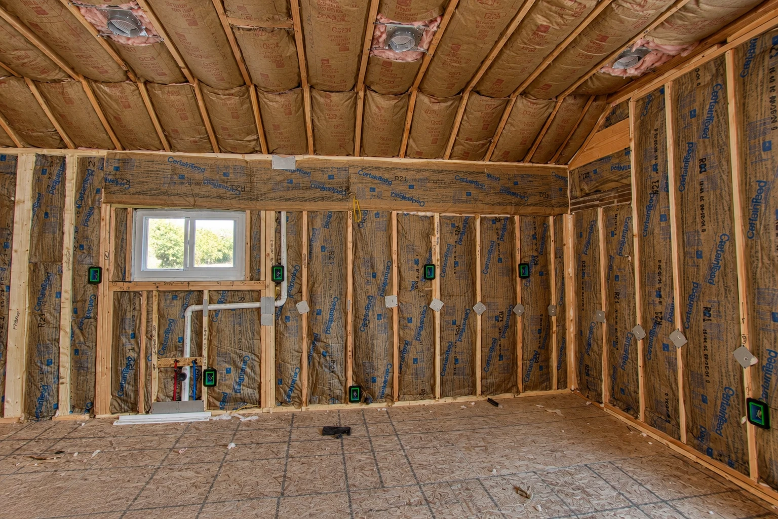 Unfinished room with fiberglass batts installed between exposed wall studs and ceiling rafters.